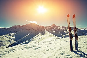two skis stood up in deep snow with a beautiful sunset over the mountains